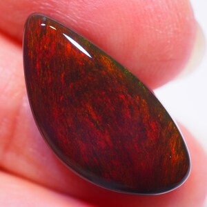 Puede incluir: Una piedra preciosa de ópalo rojo oscuro en forma de lágrima con destellos verdes y rojos.
