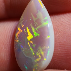 Könnte beinhalten: Ein tropfenförmiger Opal-Edelstein mit einer weißen Basis und schillernden Blitzen in Grün, Gelb und Blau.