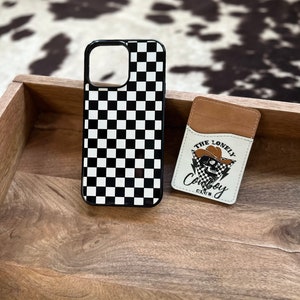 May include: Black and white checkered phone case with a black border. The case is next to a brown leather card holder with a white skull graphic and the text "The Lonely Cowboy Club".