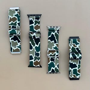May include: Four camouflage patterned watch bands with black and silver clasps. The bands are made of a stretchy material and are designed for Apple Watches.