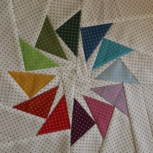 May include: A colourful quilt with a starburst pattern made from fabric with white polka dots. The fabric is arranged in a spiral pattern with each triangle a different colour.