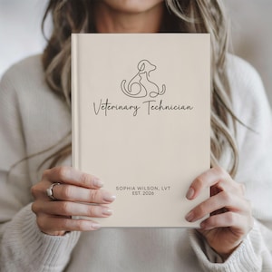 May include: A cream-colored hardcover notebook featuring a black line art illustration of a dog and a cat. The text reads Veterinary Technician, followed by the name Sophia Wilson, LVT and the establishment year EST. 2026 in a clean, dark font.