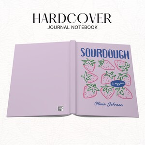 Puede incluir: Cuaderno de tapa dura abierto con una cubierta de color lila claro. La p&aacute;gina derecha presenta el texto "SOURDOUGH" en azul, con fresas rosas y la frase "is my jam". El nombre "Olivia Johnson" est&aacute; debajo.