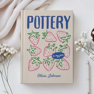 May include: A beige journal with the word "POTTERY" in blue, and pink strawberries with green leaves. The phrase "is my jam" is in a blue oval, and the name "Olivia Johnson" is written below the strawberries.