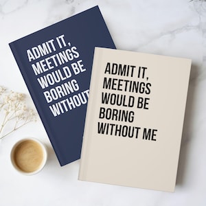 May include: Two notebooks with the text "ADMIT IT, MEETINGS WOULD BE BORING WITHOUT" and "ADMIT IT, MEETINGS WOULD BE BORING WITHOUT ME". One notebook is navy blue, the other is beige. A cup of coffee sits nearby.