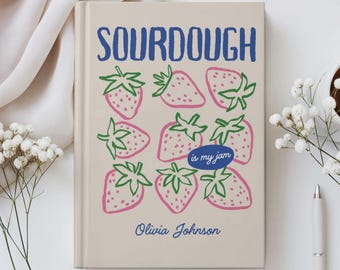May include: A beige journal with the word "SOURDOUGH" in blue, above a pattern of pink strawberries with green stems. The text "is my jam" is in a blue oval, and the name "Olivia Johnson" is below the strawberries.