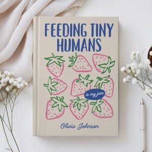 May include: A hardcover book with a beige cover featuring the blue text FEEDING TINY HUMANS, a pattern of pink strawberries with green leaves, a blue oval with the text is my jam, and the author name Olivia Johnson in blue script font.