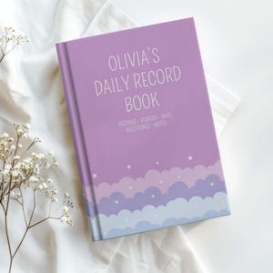 May include: A purple hardcover daily record book with white text that reads OLIVIA'S DAILY RECORD BOOK, FEEDINGS, DIAPERS, NAPS, MILESTONES, NOTES. The bottom features a layered cloud pattern in shades of purple and blue with small white stars.