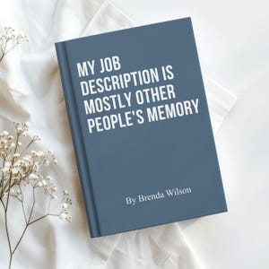 May include: A blue hardcover book with white text that reads, My Job Description Is Mostly Other People's Memory, and By Brenda Wilson. The book is positioned at an angle, featuring a clean, bold sans-serif font for the title.