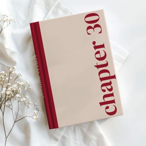 May include: A hardcover book with a light beige cover and a burgundy spine. The words "chapter 30" are printed vertically in burgundy on the cover. The book is resting on a white, textured surface, with small white flowers in the corner.