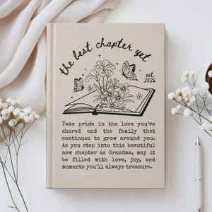 May include: A beige journal with the text "the best chapter yet" and "est. 2026" in black script. The cover features a floral and butterfly design above an open book. The journal includes a message about family and love.