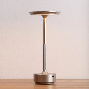 May include: A silver modern table lamp with a round base and a circular light fixture. The lamp has a textured stem and a USB charging port on the base.
