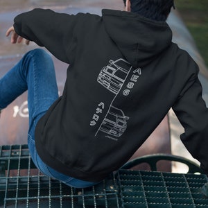 May include: Black hoodie with a white outline of a car on the back. The car is split in half with the top half facing one way and the bottom half facing the other way. The text "AE86" is written vertically on the right side of the car and the text "ハチロク" is written vertically on the left side of the car.