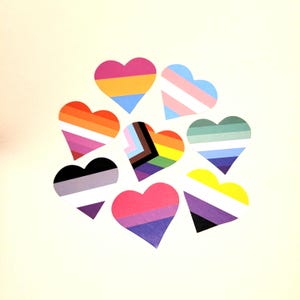 May include: Eight heart-shaped stickers, each with a unique design representing different LGBTQ+ identities. The hearts are arranged in a circular pattern against a cream background. The stickers feature a variety of bright colours.