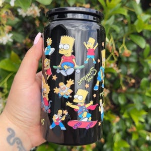Pode incluir: Caneca preta com um design com personagens dos Simpsons. A caneca tem uma tampa preta e um acabamento brilhante. O design inclui Bart Simpson andando de skate e as palavras "The Simpsons".