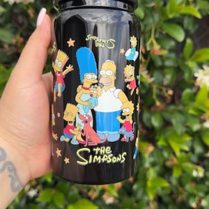 Pode incluir: Pote preto com uma ilustra&ccedil;&atilde;o colorida da fam&iacute;lia Simpson. O pote tem um acabamento brilhante e &eacute; rodeado por um fundo de folhas verdes. O logotipo dos Simpsons &eacute; exibido no pote.