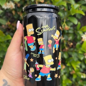 Pode incluir: Caneca preta com ilustra&ccedil;&otilde;es de Bart Simpson da s&eacute;rie de desenhos animados Os Simpsons. A caneca tem uma tampa preta e as palavras "The Simpsons" em amarelo. Bart &eacute; retratado em v&aacute;rias poses, com estrelas espalhadas pelo design.