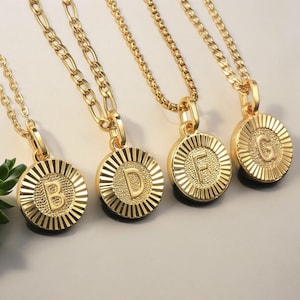 May include: Four gold necklaces with round pendants featuring the letters B, D, F, and G. Each pendant has a textured, sunburst design.