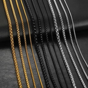 May include: A variety of gold, silver, and black chain necklaces. The chains are arranged in rows on a black surface.