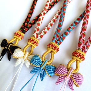 May include: Four colorful braided lanyards with butterfly charms. The lanyards are red, white, and blue, black and red, blue and green, and pink and red. The butterfly charms are black, white, blue, and pink.
