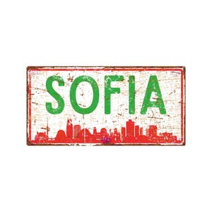May include: A rectangular metal sign with the word "SOFIA" in large green letters. The sign has a distressed, vintage look with a red skyline at the bottom. The background is white with brown and green accents.