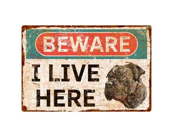 May include: A rusty metal sign with a blue and red border. The sign reads "Beware I Live Here" and features a brown and black dog's head.