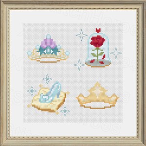 Peut inclure: Broderie au point de croix repr&eacute;sentant quatre ic&ocirc;nes de contes de f&eacute;es : un diad&egrave;me, une rose sous cloche, un chausson de verre sur un coussin et une couronne dor&eacute;e. L'&oelig;uvre est encadr&eacute;e dans un cadre en bois brun clair. Le fond est une grille blanche.