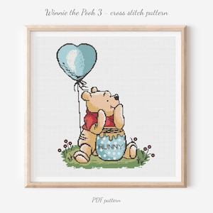 Puede incluir: Patrón de punto de cruz con Winnie the Pooh sosteniendo un globo azul en forma de corazón. Pooh lleva una camisa roja y está sentado junto a un tarro de miel que dice "Hunny". La imagen está enmarcada e incluye el texto "Winnie the Pooh 3 - cross stitch pattern" y "PDF pattern".