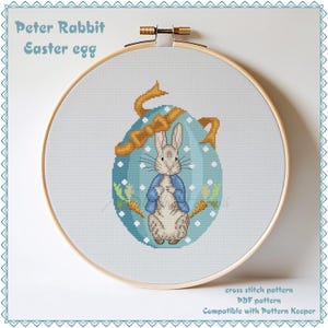Puede incluir: Patrón de punto de cruz de Peter Rabbit en un huevo de Pascua azul con una cinta amarilla. El patrón es compatible con Pattern Keeper.