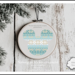 以下が含まれることがあります： 青と白のノルウェーのセーターデザインのミッキーマウスの頭のクロスステッチパターン。パターンは白い木製の背景に丸い刺繍枠に表示されています。テキスト「Norwegian Mickey ornament」は枠の下にあります。テキスト「XStitch Heroes」は右下の吹き出しの中にあります。
