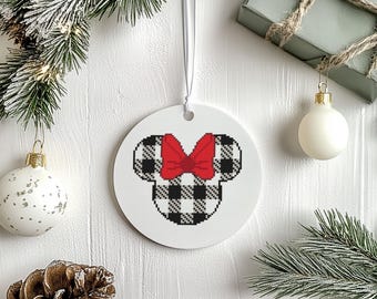 May include: A white, round Christmas ornament featuring a black and white buffalo plaid Mickey Mouse head with a red bow. The ornament hangs from a white ribbon. Festive holiday decor.