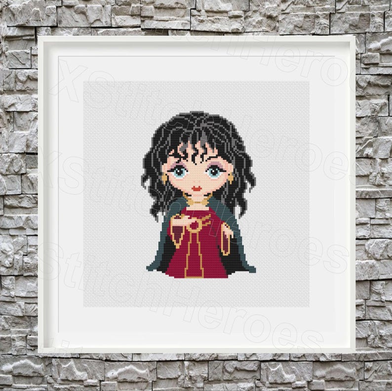 May include: A framed cross-stitch of a cartoon woman with black curly hair, blue eyes, and a red dress. She wears a dark green cape and gold jewelry. The artwork is displayed in a white frame against a gray brick wall.