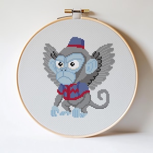 May include: Cross-stitch embroidery of a cartoon monkey with wings, wearing a blue and red outfit and hat. The monkey has a stern expression and is set in a wooden embroidery hoop.