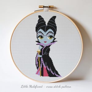 May include: A cross-stitch pattern of a cartoon Maleficent character, featuring a black dress, horns, and staff. The design is set within a wooden embroidery hoop, with the text "Little Maleficent - cross stitch pattern" at the bottom.