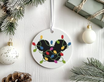 Peut inclure: Ornement de Noël rond et blanc avec une silhouette noire de tête de souris ornée de guirlandes lumineuses colorées. L'ornement est suspendu à un ruban blanc. D'autres décorations de Noël sont en arrière-plan.
