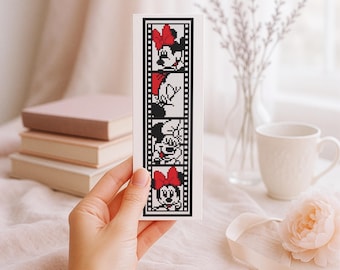 Może przedstawiać: Biała zakładka do książki z haftem krzyżykowym przedstawiającym Minnie Mouse w stylu taśmy filmowej. Czarno-biały wzór zawiera twarz Minnie i czerwoną kokardę. Zakładka jest trzymana na tle miękkiego, neutralnego tła.