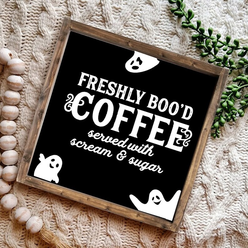 May include: A black wooden sign with white text that reads "Freshly Boo'd Coffee served with scream & sugar". The sign is decorated with three white ghost silhouettes.
