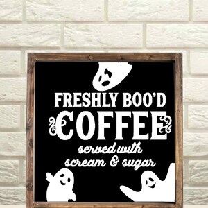 May include: A black framed sign with white text that reads "Freshly Boo'd Coffee served with scream & sugar". There are three white ghost silhouettes on the sign.