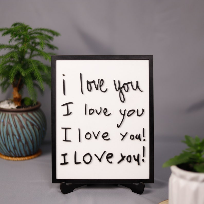 May include: A black framed whiteboard with the words "i love you" written on it four times, with each line increasing in size and intensity. The whiteboard is standing on a black stand.