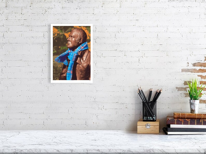 ‘Hap Up, Rabbie!’ art print, A4 size, unframed, shown on a wall. A statue of Scots bard Robert (Rabbie) Burns with a colourful scarf wrapped around it.