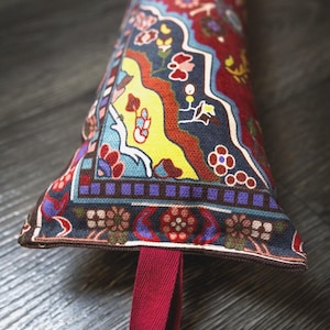 Può includere: Un paraspifferi in tessuto lungo e triangolare caratterizzato da un dettagliato motivo floreale e geometrico multicolore nei toni del rosso, giallo, blu e viola. L'articolo include un passante in tessuto rosso tinta unita a un'estremità.