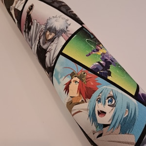 May include: Rolled fabric with a comic book style design. The panels display anime characters in different poses and settings. The colour palette includes white, black, blue, red, and green. The fabric is rolled up.