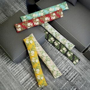 Può includere: Cinque fermaporte a forma di cuscino con motivi floreali. I cuscini sono di vari colori, tra cui rosso, blu, giallo, nero e bianco. I cuscini sono tutti in tessuto e hanno un motivo floreale.