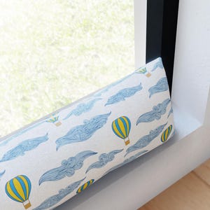 May include: A white draft stopper with a blue and yellow hot air balloon pattern. The draft stopper is designed to prevent drafts from entering a room.