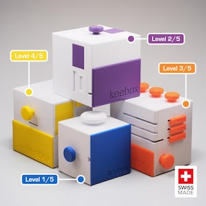 Puede incluir: Un conjunto de cubos de rompecabezas blancos con detalles en morado, amarillo, azul y naranja. Cada cubo tiene un diseño diferente, con perillas, deslizadores y el texto "keebox". Los cubos están etiquetados con los niveles 1/5, 2/5, 3/5 y 4/5.