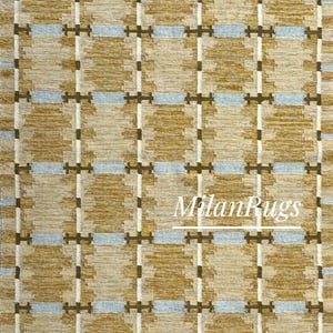 Puede incluir: Una alfombra tejida con un diseño geométrico. La alfombra presenta un diseño de cuadrícula con cuadrados alternos en beige y marrón, acentuados por líneas blancas y celeste. El texto "Milan Rugs" es visible.