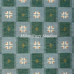 May include: A woven rug with a repeating pattern of squares in teal and green. Each square contains a cross-like design in white and tan. The text "MilanRugs Studios" is visible on the rug.