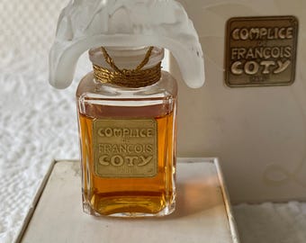 May include: A vintage "Complice de Francois Coty" perfume bottle with a frosted glass stopper. The rectangular bottle has a gold label and a gold-coloured string around the neck. The perfume is amber-coloured. The box is white with gold lettering.