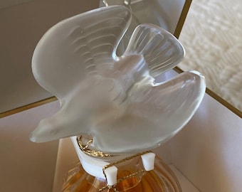 May include: A clear glass bottle with a gold stopper shaped like a dove. The bottle is filled with a golden liquid.