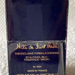 Puede incluir: Una caja azul con letras doradas para el perfume Niki de Saint Phalle. La caja tiene el texto "This exclusive formula contains: SD Alcohol 39-C. Fragrance. Water." y "No. 6202 Made in France Parfums Niki de Saint Phalle U.S. Distributor Jacqueline Cochran, Inc. New York, N.Y. 10111 6202-402280".